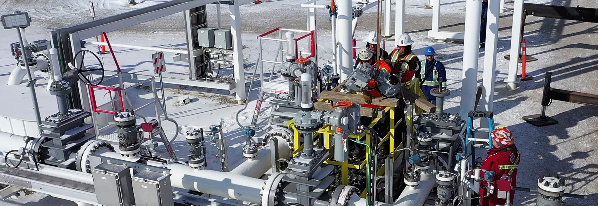 Aerial view of a team of pipeline technicians as they prepare to launch a tool in winter from inside a fenced pipeline station.