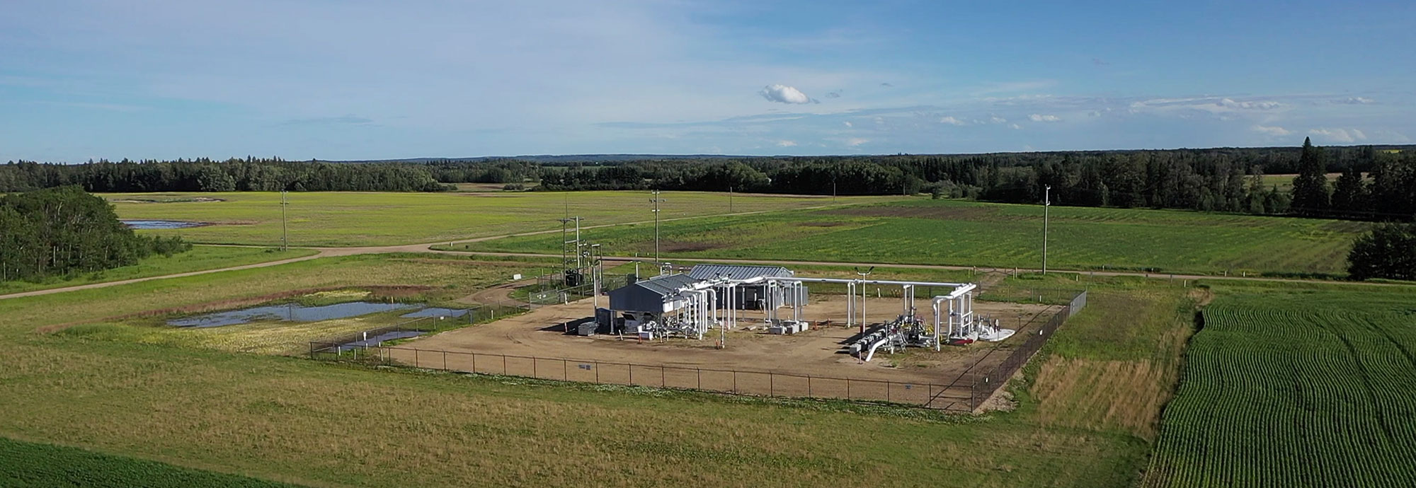 Aerial view of pipeline station surrounded by grass, fields, and forested areas behind the station.