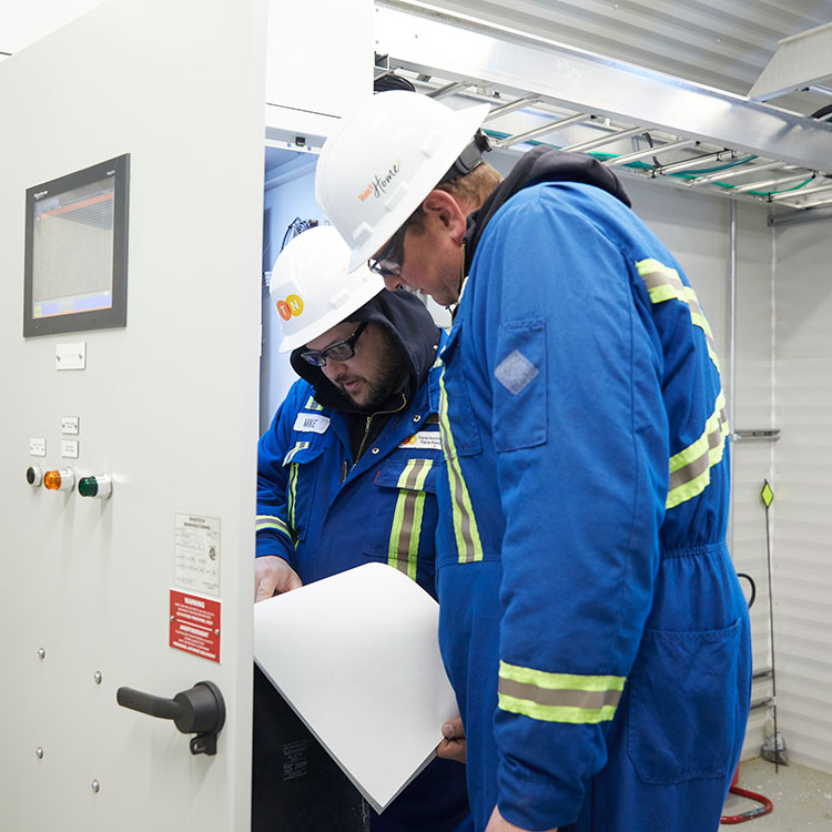 Two pipeline technicians review documentation for a station control panel.