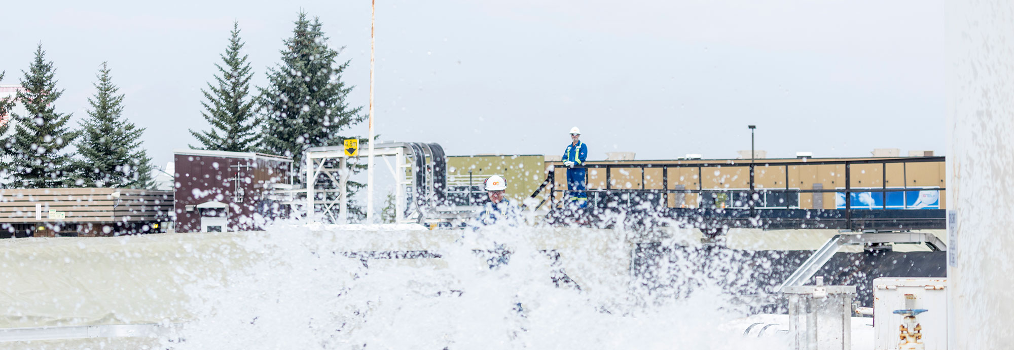 A pipeline technician observes as his colleague deploys fire-retardant foam which you can see spraying towards the camera lens.