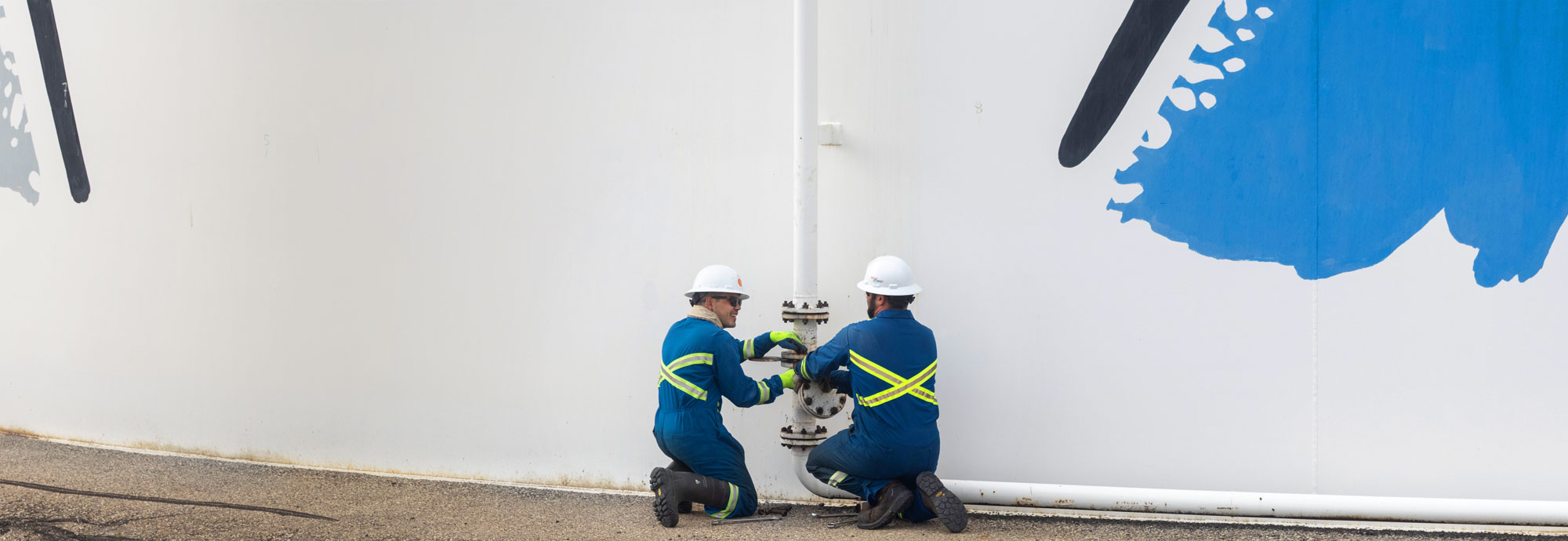 Two pipeline technicians are kneeling, adjusting a valve on a fuel tank.