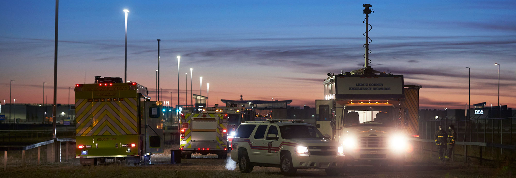 Emergency response vehicles are parked in a field as dawn begins to break.