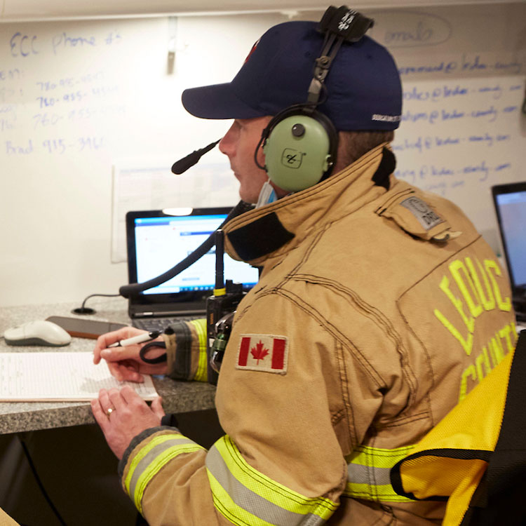 A Leduc County first responder wearing a ballcap and headset takes notes inside the response trailer.