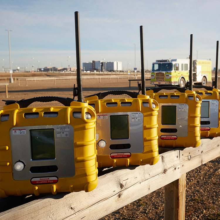 Emergency communication devices lined up along a fence, with a fire truck visible in the background.