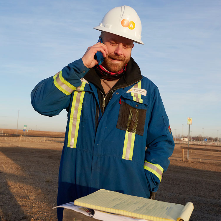 A TNPI pipeline technician in his blue coveralls and safety hat speaks on a mobile phone.