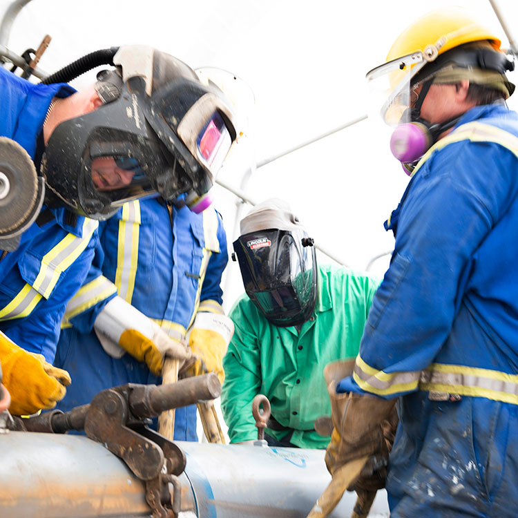 Welders work on an exposed segment of pipeline during regular maintenance activity.