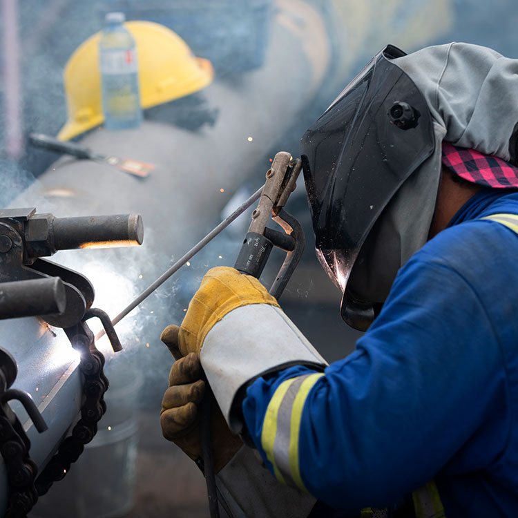 Welder working on a pipeline weld, wearing personal protective equipment.