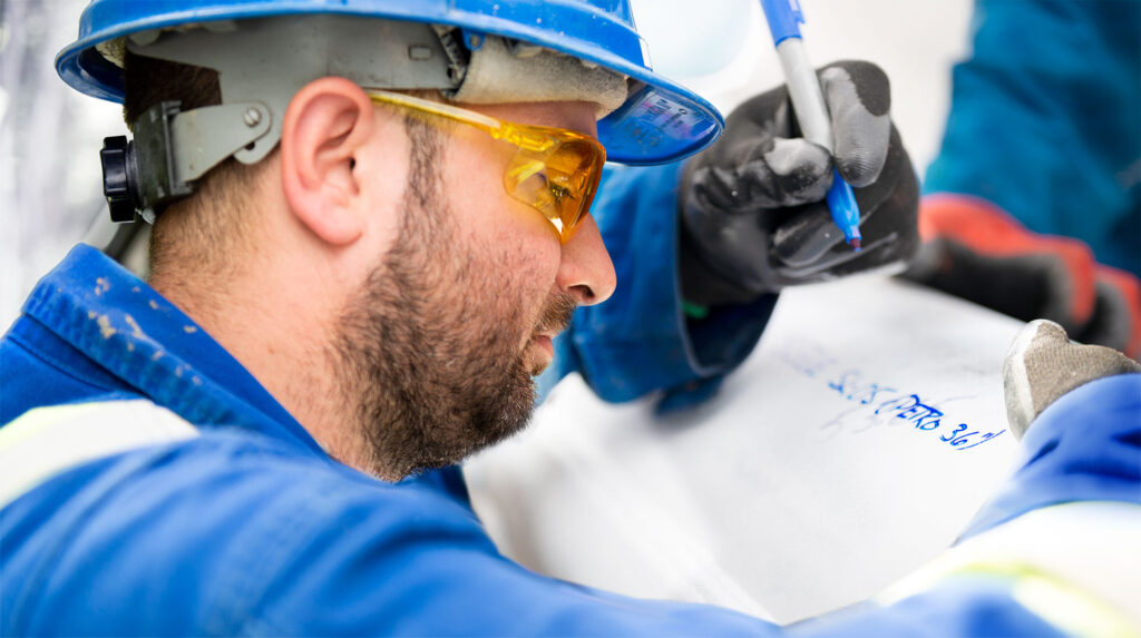 Close up of employee in hard hat and saftey glasses writing with a sharpie