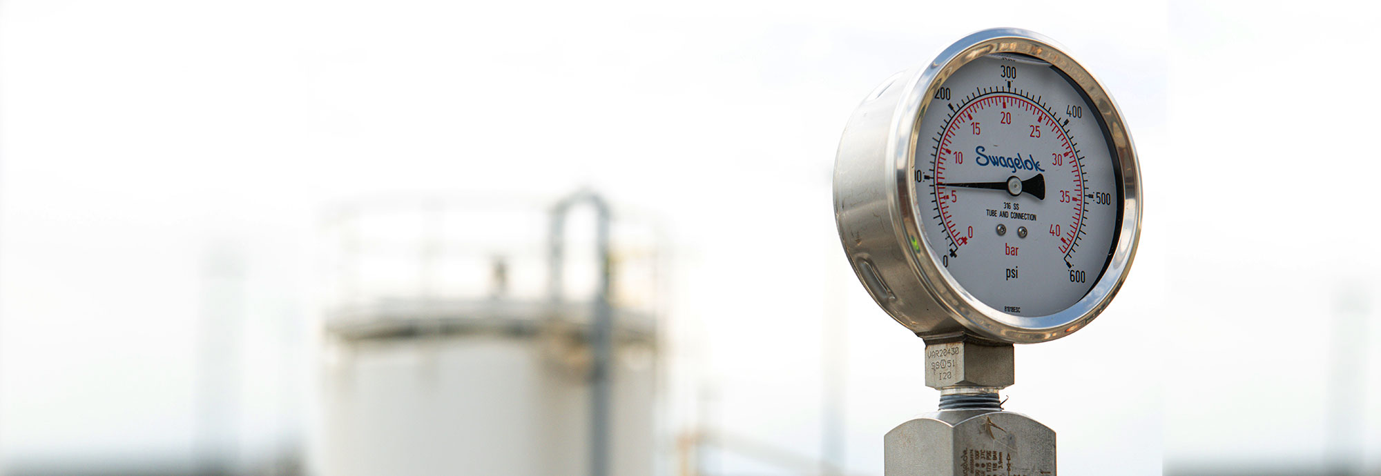 Pipeline instrumentation with product tank blurred in the background.