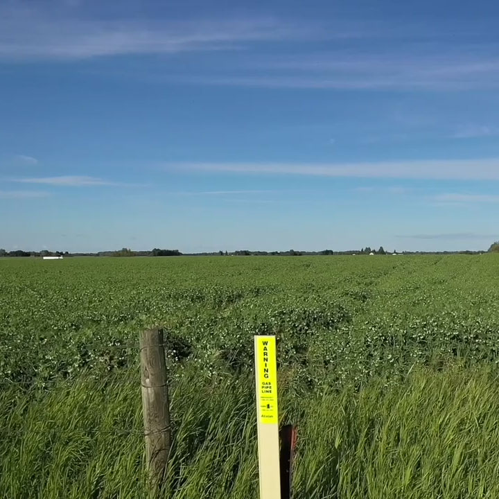 Pipeline marker near a fence post along agricultural land.