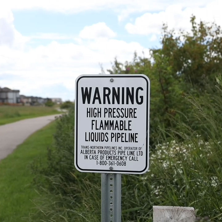 White APPL pipeline marker with English writing next to a bike path in a residential community.